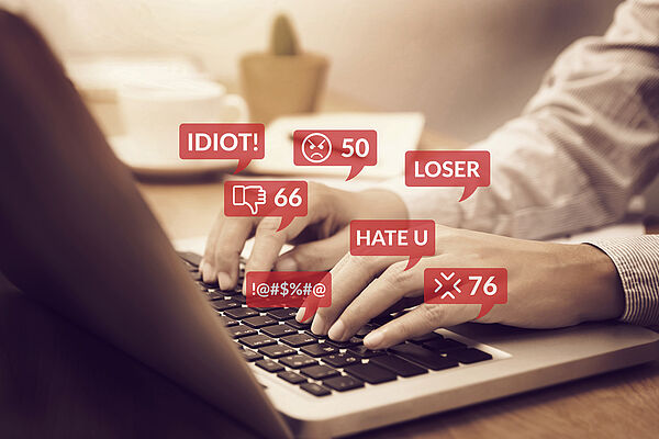 Das Bild zeigt einen Internetnutzer, der am Laptop Hass-Kommentare tippt