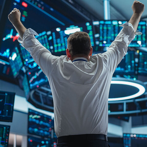 Ein Börsenmanager reißt die Hände hoch und jubelt über einen erfolgreichen Investmenttag. 