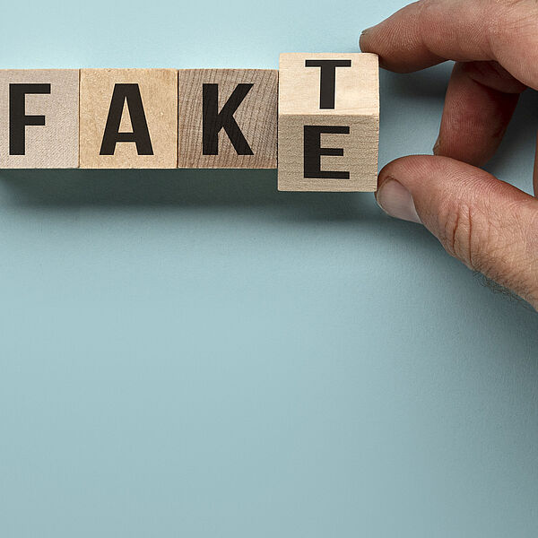 Zwei Finger drehen Holzwürfel mit Buchstaben so um, dass aus dem Wort Fake das Wort Fakt wird