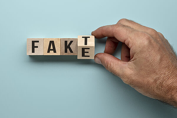 Zwei Finger drehen Holzwürfel mit Buchstaben so um, dass aus dem Wort Fake das Wort Fakt wird
